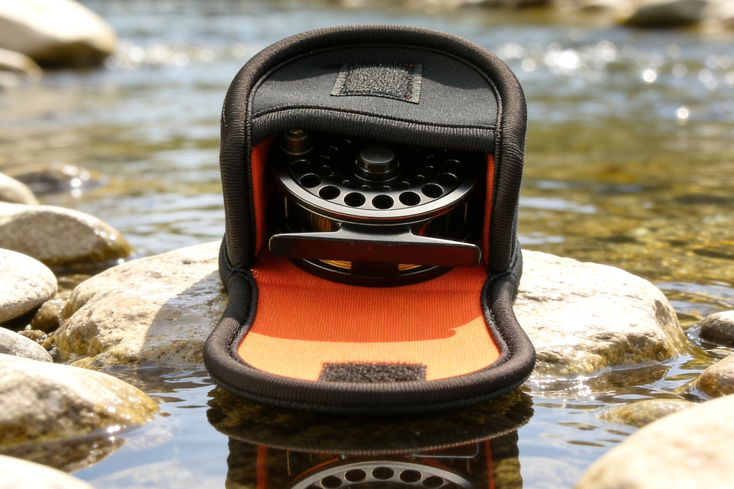 Fly fishing reel in a protective case on a rock by a stream