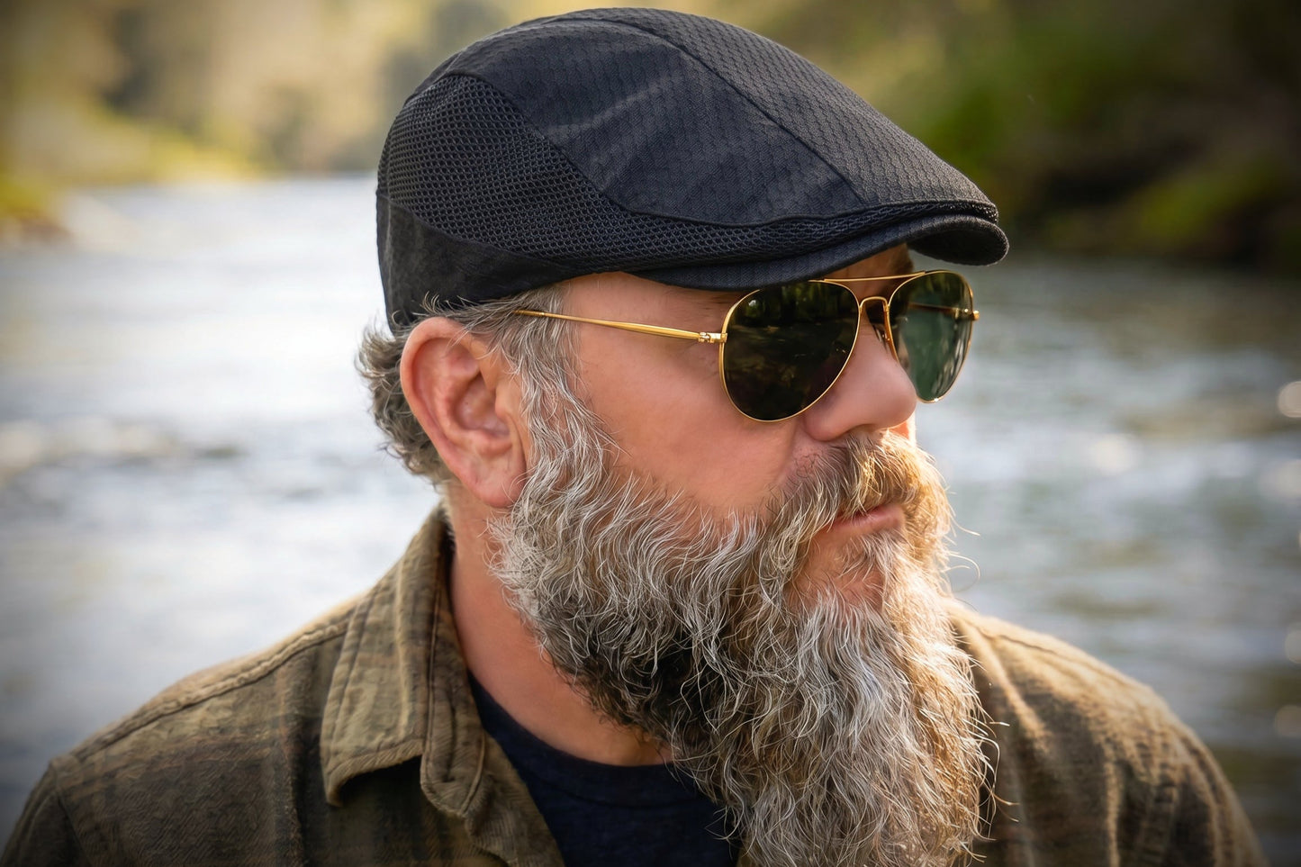 Man with a beard wearing sunglasses and a cap by a river