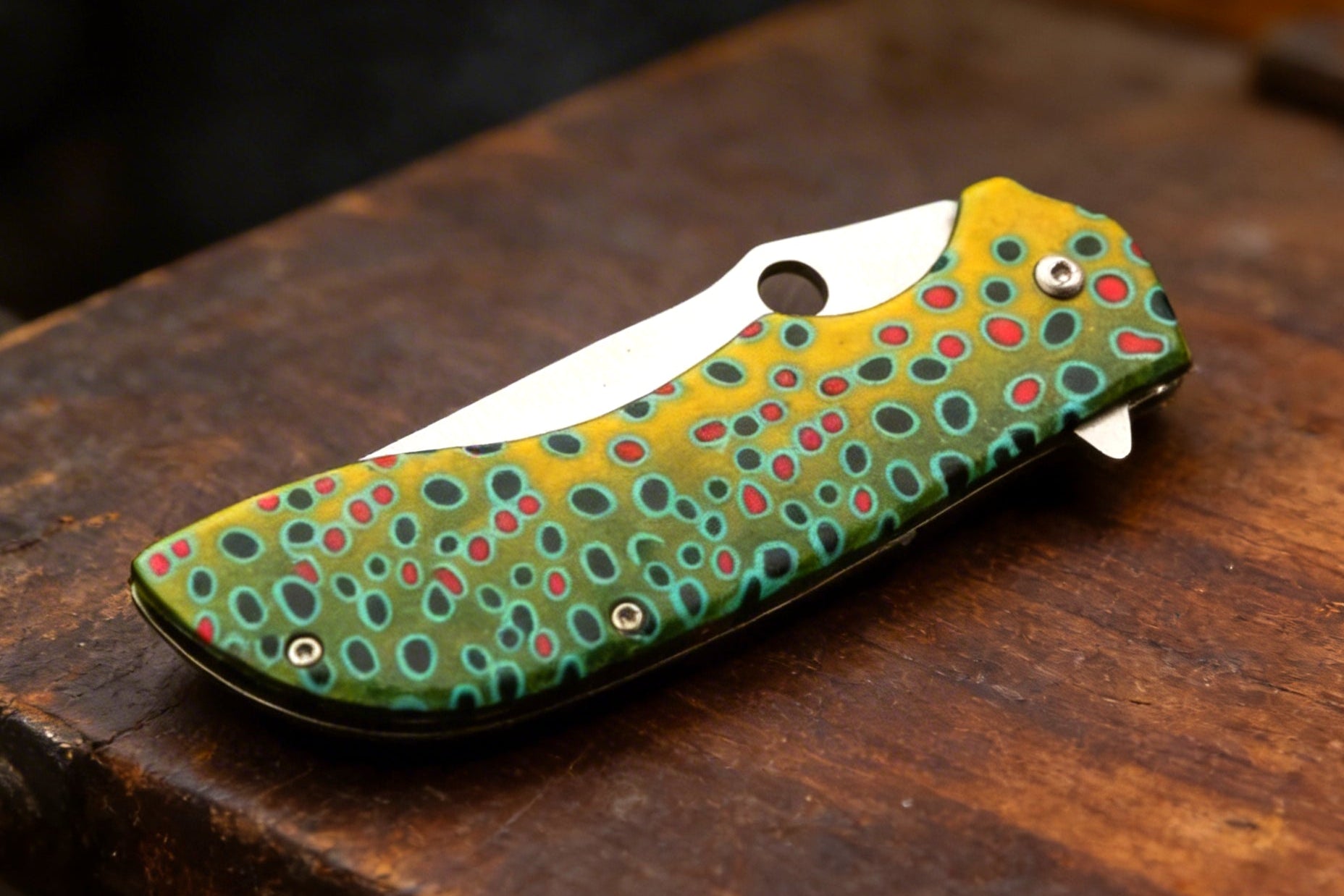 Fishing-themed pocket knife with a green and yellow pattern on a wooden surface